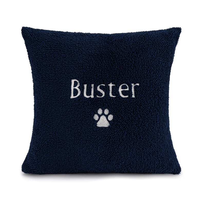 May include: A navy blue plush pillow with the name "Buster" embroidered in white with a white paw print below it.
