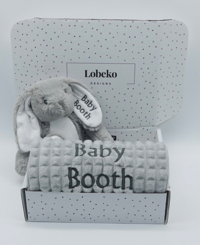 May include: A grey and white plush bunny toy and a grey blanket with the name "Baby Booth" embroidered on it. The items are in a white box with a grey polka dot pattern and the text "Lobeko Designs".