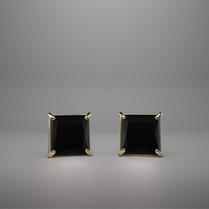 Pu&ograve; includere: Un paio di orecchini a lobo con gemme nere a taglio quadrato incastonate in griffe di metallo dorato. Ogni orecchino presenta una pietra scura sfaccettata con una silhouette geometrica netta, fissata da quattro griffe metalliche angolari.