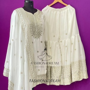 May include: White embroidered dress with a long, flowing top and a flared skirt. The dress is decorated with silver sequins and beads. The dress is on a mannequin against a purple background. The text "FASHION4DREAM" is visible on the dress.