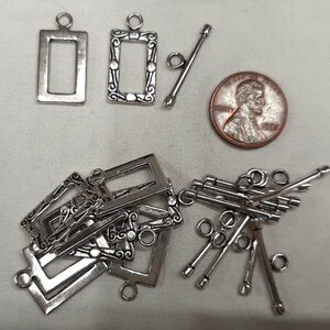 May include: Silver metal jewelry clasps and toggle bars. The clasps are rectangular, some with decorative edges. A penny is included for size reference. The clasps have a loop for attaching to jewelry.