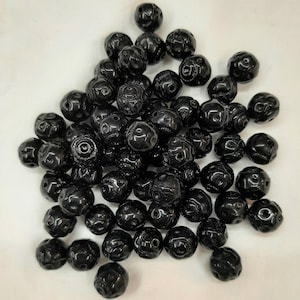 May include: A pile of black round beads with intricate designs. The beads are made of a smooth, polished material and have a glossy finish.