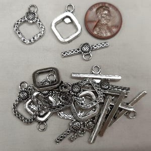Pode incluir: Uma coleção de fechos e conectores de joias prateados, incluindo designs quadrados e florais. Uma moeda é incluída para referência de tamanho. Os fechos variam em forma e estilo, adequados para fazer joias e projetos de artesanato.