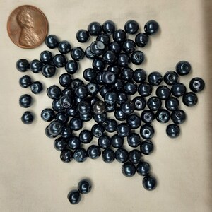 May include: A large pile of dark blue round beads. The beads are smooth and shiny.