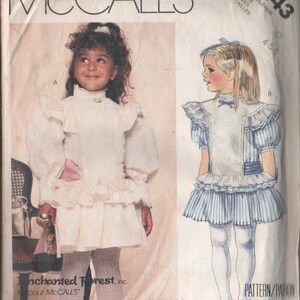 May include: A vintage sewing pattern for a girl's dress. The pattern is for sizes 4-5-6 and is from McCall's. The pattern features two different styles of dresses, one with a white ruffled skirt and the other with a blue and white striped skirt. The pattern is called "Enchanted Forest" and is for McCall's.