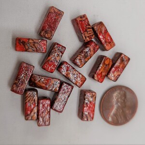 May include: A collection of small, rectangular, red and brown patterned tiles. The tiles are arranged in a random pattern on a white surface.