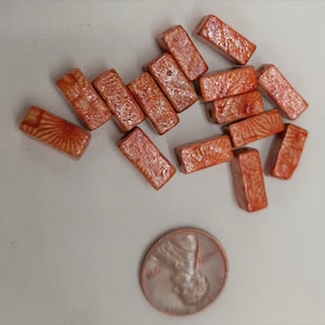 May include: A group of 13 rectangular ceramic tiles with a light orange glaze and a white pattern. The tiles are approximately 1 inch long and 1/2 inch wide.