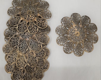 May include: A set of six gold-colored metal filigree doilies. The doilies are layered on top of each other, creating a cascading effect. The doilies are intricate and delicate, with a floral design.