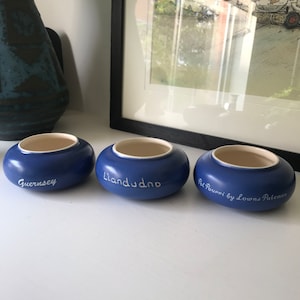 May include: Three blue ceramic bowls with white lettering. The bowls are labelled "Guernsey", "Llandudno", and "Pot Pourri by Lowns Patemam".