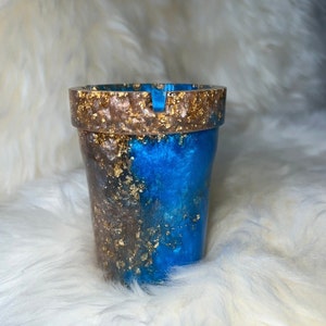May include: A blue and gold ashtray with a unique swirl design. The ashtray is made of resin and has a gold fleck finish.