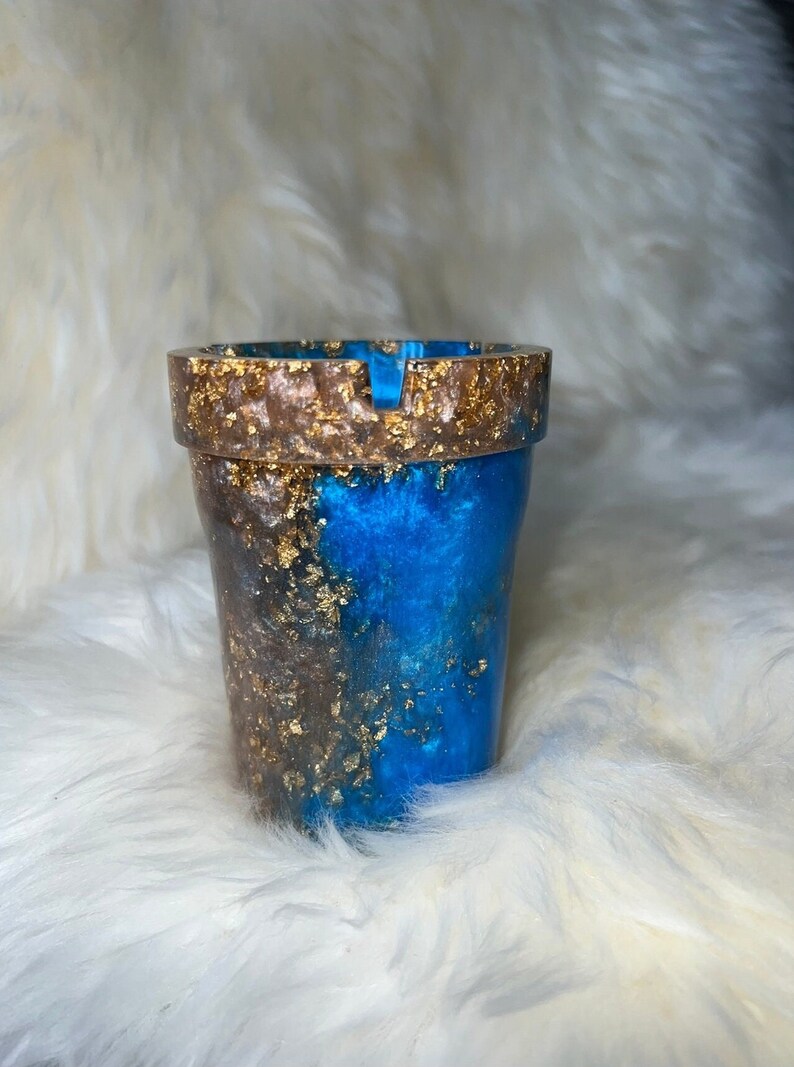 May include: A blue and gold ashtray with a unique swirl design. The ashtray is made of resin and has a gold fleck finish.