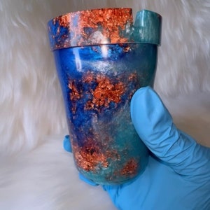May include: A blue and green resin ashtray with a copper metallic finish. The ashtray has a wide, round opening and a small lip around the top.