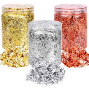 May include: Three jars of gold, silver, and copper leaf flakes. The jars are clear plastic with lids. The flakes are loose and scattered around the jars.