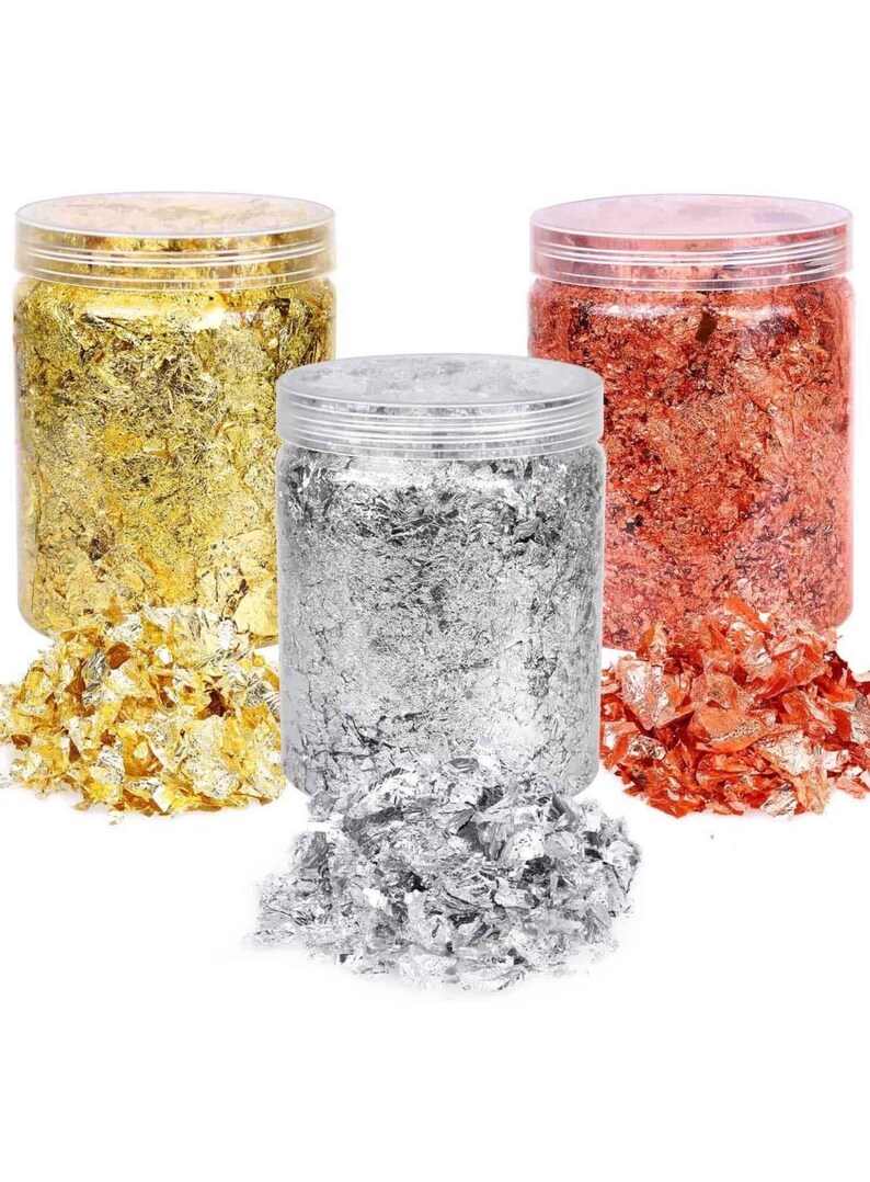 May include: Three jars of gold, silver, and copper leaf flakes. The jars are clear plastic with lids. The flakes are loose and scattered around the jars.