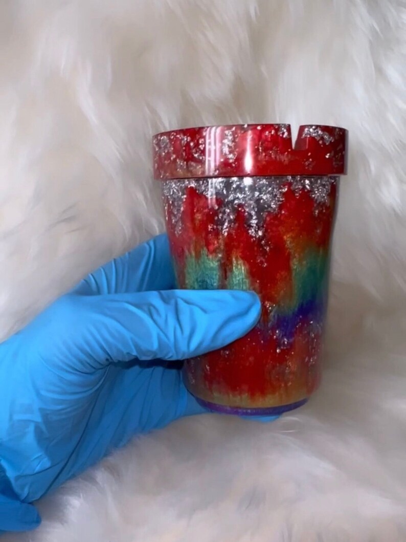 May include: A red, green, and purple tie-dye ashtray with silver glitter accents. The ashtray is made of resin and has a round shape.