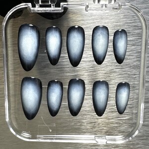 May include: A set of ten false nails in a clear plastic case. The nails are a light gray color with a black ombre effect.