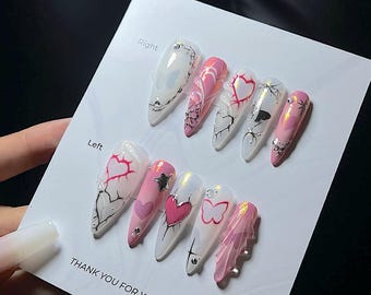 May include: A set of ten long, pointed artificial nails. Each nail is painted with a unique design, featuring hearts, butterflies, and abstract patterns in white, pink, and silver. The nails are arranged on a white card with the text "THANK YOU FOR YOUR ORDER".