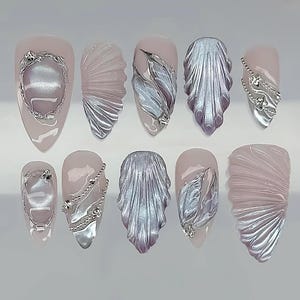 May include: A set of ten artificial nails in various designs. Each nail features a pale pink base with silver embellishments. Designs include textured silver fan shapes, feather-like details, and ornate silver accents with rhinestones.