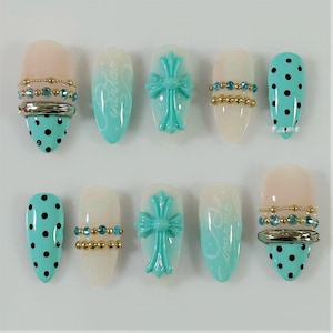 May include: A set of ten press-on nails featuring a mix of designs including turquoise polka dots, turquoise cross emblems, gold and turquoise bead accents, and white to turquoise gradient backgrounds with cursive script text.