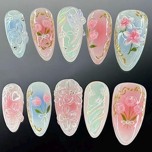 May include: A collection of ten artificial nails, each with a unique design. The nails showcase floral, butterfly, and abstract patterns. They are painted in pastel shades of pink, blue, and green, with gold detailing. The nails are oval-shaped.