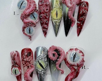 May include: A set of ten long, pointed artificial nails with a horror theme. Designs include realistic-looking eyeballs, tentacles, and blood-like patterns in shades of red, pink, and metallic colors.