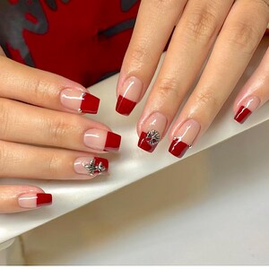 May include: Close-up of manicured nails with a red French tip design. Some nails feature silver embellishments. The nails are square-shaped with a clear base and a bold red tip.