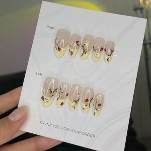 May include: A set of almond-shaped false nails with a clear base and yellow tips. Each nail is decorated with a floral design featuring red ladybugs and white flowers. The card reads "THANK YOU FOR YOUR ORDER."