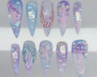 May include: A set of ten long, pointed artificial nails. Each nail features a unique design with shades of blue, purple, and iridescent accents. Some nails have bubble-like embellishments, while others showcase intricate patterns and textures.