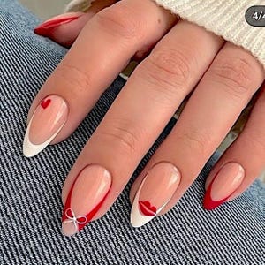 A close-up of a person's hand with long, red-painted fingernails and a bow on the tip.