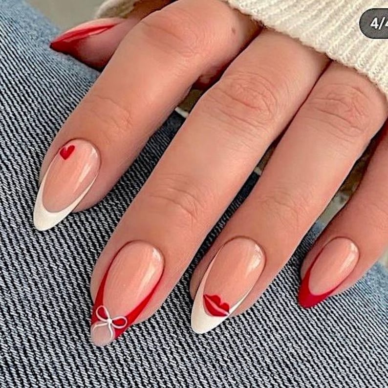 A close-up of a person's hand with long, red-painted fingernails and a bow on the tip.