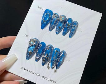 May include: A set of blue press-on nails with silver embellishments. The nails feature a glossy finish and are adorned with crosses, stars, and other decorative elements. The card reads "Right" and "Left" with the text "THANK YOU FOR YOUR ORDER".