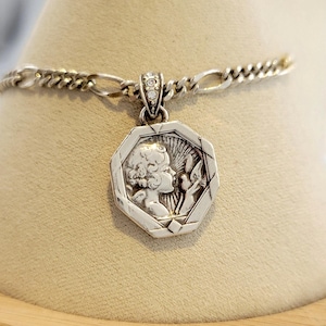 K&ouml;nnte beinhalten: Silberfarbene Anh&auml;ngerkette mit achteckigem Anh&auml;nger, der das Profil einer Person und florale Elemente zeigt. Der Anh&auml;nger h&auml;ngt an einer Silberkette. Der Anh&auml;nger hat eine kleine Schlaufe mit klaren Steinen.