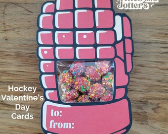 May include: Pink hockey glove Valentine's Day card with a clear plastic window filled with colorful candy. The card has the words "to:" and "from:" printed on it.  "Titles and Jotters" is printed in the top right corner.