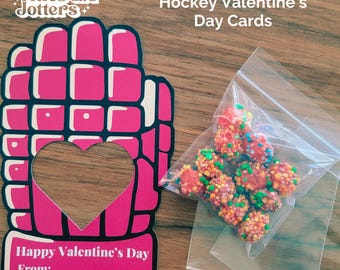May include: Pink hockey glove Valentine's Day card with a heart cut out. The card says "Happy Valentine's Day From:". A small bag of colorful candy is in the background.