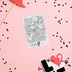 Image of a 4x6 valentine featuring a heart filled image for your valentine to color.  Valentine is primarily black and white. Image background is a heart confetti and valentine party favors. By Titles and Jotters.