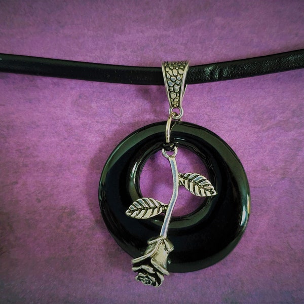 circular black pendant with fallen rose on a faux leather choker.