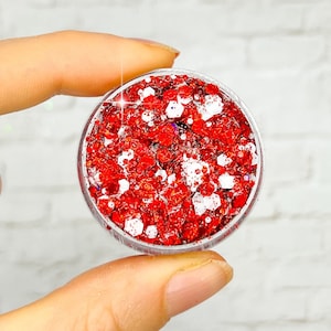 May include: A small clear jar filled with red and white glitter. The glitter is a mix of small and large pieces.