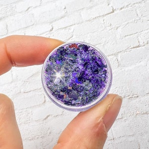 May include: A small clear jar filled with purple and silver glitter.