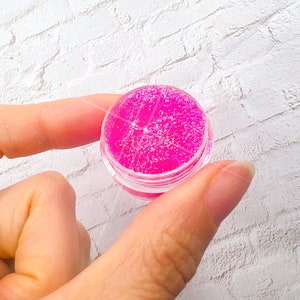 May include: A small clear jar filled with pink glitter.