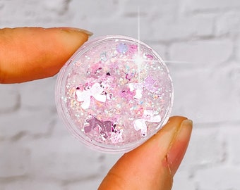 May include: A small clear jar filled with pink and white glitter and iridescent holographic glitter. The glitter is in the shape of stars and hearts.