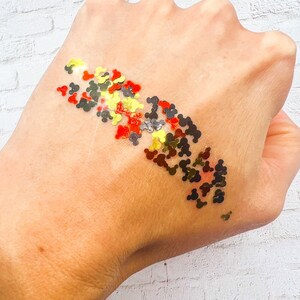 May include: A hand with a design of red, gold, and black Mickey Mouse heads on the skin.