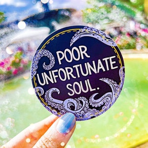 May include: A round sticker with a dark blue background and a gold border. The sticker features a purple octopus design and the text "Poor Unfortunate Soul."