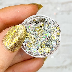 May include: A small clear jar filled with silver and gold glitter with star shapes. The glitter is iridescent and has a holographic effect.