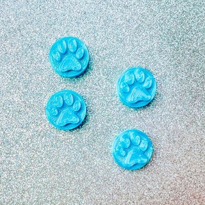 May include: Four light blue paw print shaped resin cabochons on a silver glitter background.