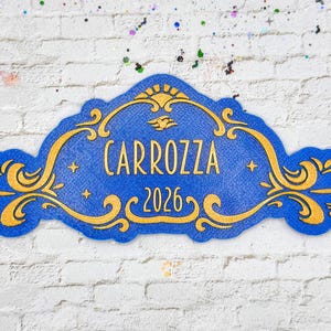 May include: A blue decorative sign with gold filigree and the word "CARROZZA" above the number "2026". The sign has a textured appearance and is set against a white brick wall.