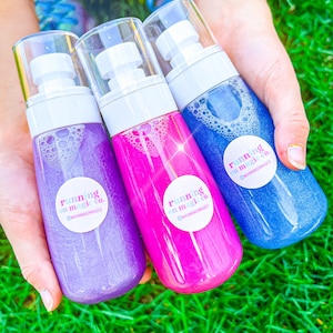 Peut inclure: Trois flacons de liquide paillet&eacute; iridescent en violet, rose et bleu. Chaque flacon est dot&eacute; d'un bouchon pompe blanc et d'une &eacute;tiquette circulaire blanche avec le texte "running on magic co." et un identifiant de m&eacute;dias sociaux.