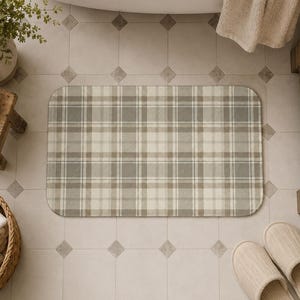 May include: A rectangular bath mat featuring a neutral-toned plaid pattern in shades of beige, cream, and soft gray. The mat has rounded corners and a consistent grid design composed of intersecting horizontal and vertical lines of varying widths.