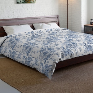 May include: A white and blue floral duvet cover with a white background and blue floral pattern. The duvet cover is on a bed with a wooden headboard and a brown rug.