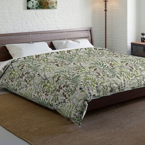 May include: A white and green duvet cover with a botanical print featuring ferns, leaves, and flowers. The duvet cover is on a bed with a wooden headboard and a brown rug.