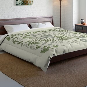 May include: A bed with a dark brown wooden frame and a beige comforter featuring a green botanical pattern. The room has a white brick wall, a brown rug, and a floor lamp. A painting with gold and green circles hangs on the wall.